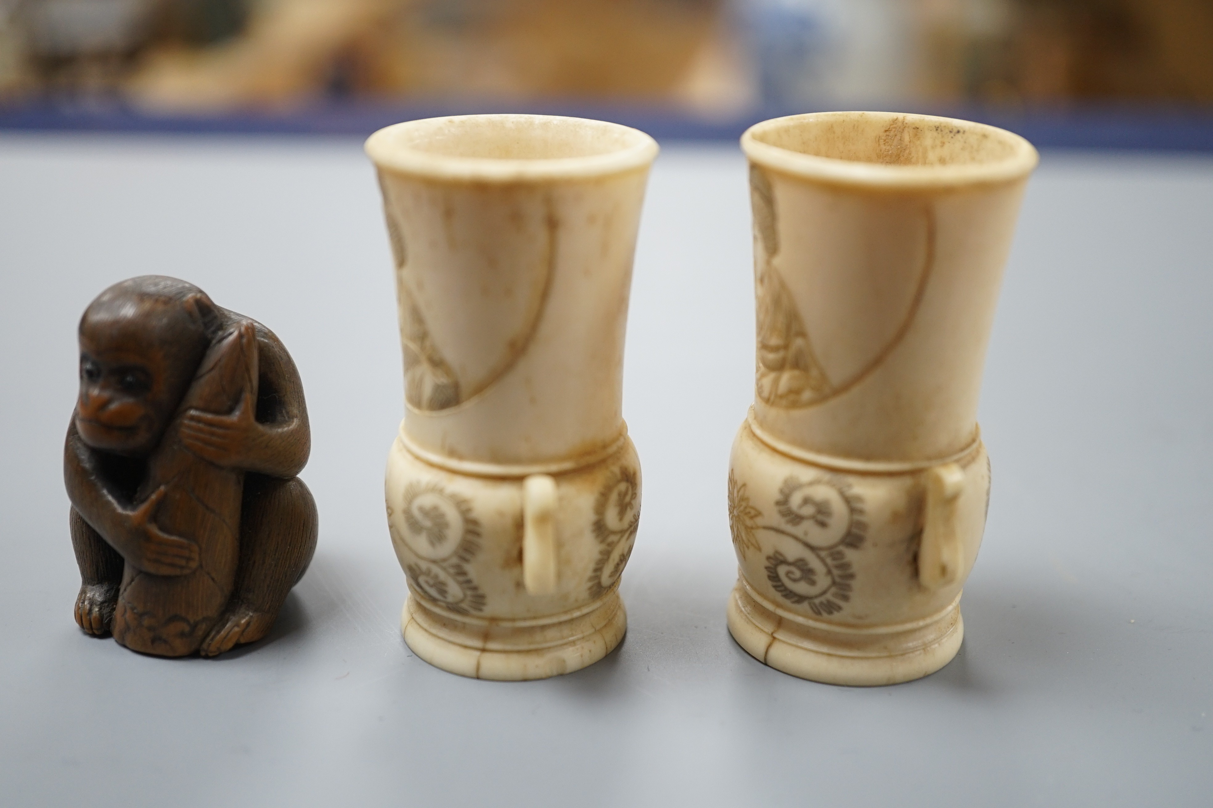 A pair of early 20th century Japanese miniature ivory vases, 5.3 cm, engraved with a lady and a wood netsuke in the form of a monkey holding a bamboo shoot (3)